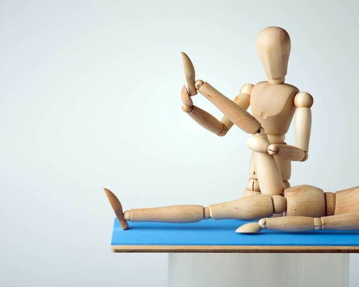 Symbolbild mit zwei Holzfiguren als Patient und Therapeut. Therapeut zeigt Übung am Kniegelenk