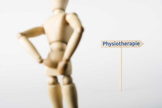 Symbolbild einer Holzfigur, die sich den Rücken hält und einem Wegweiser zur Physiotherapie folgt